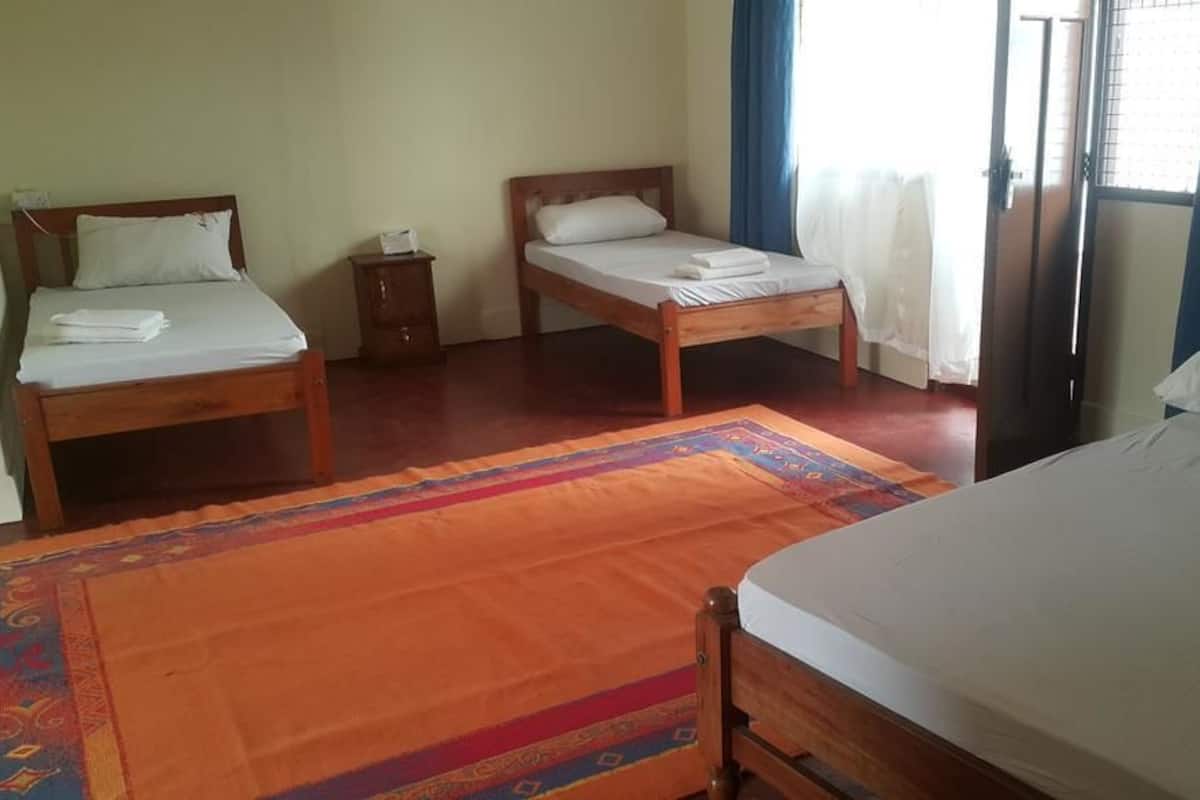 A room with three wooden beds, a small wooden nightstand, and a colorful rug.