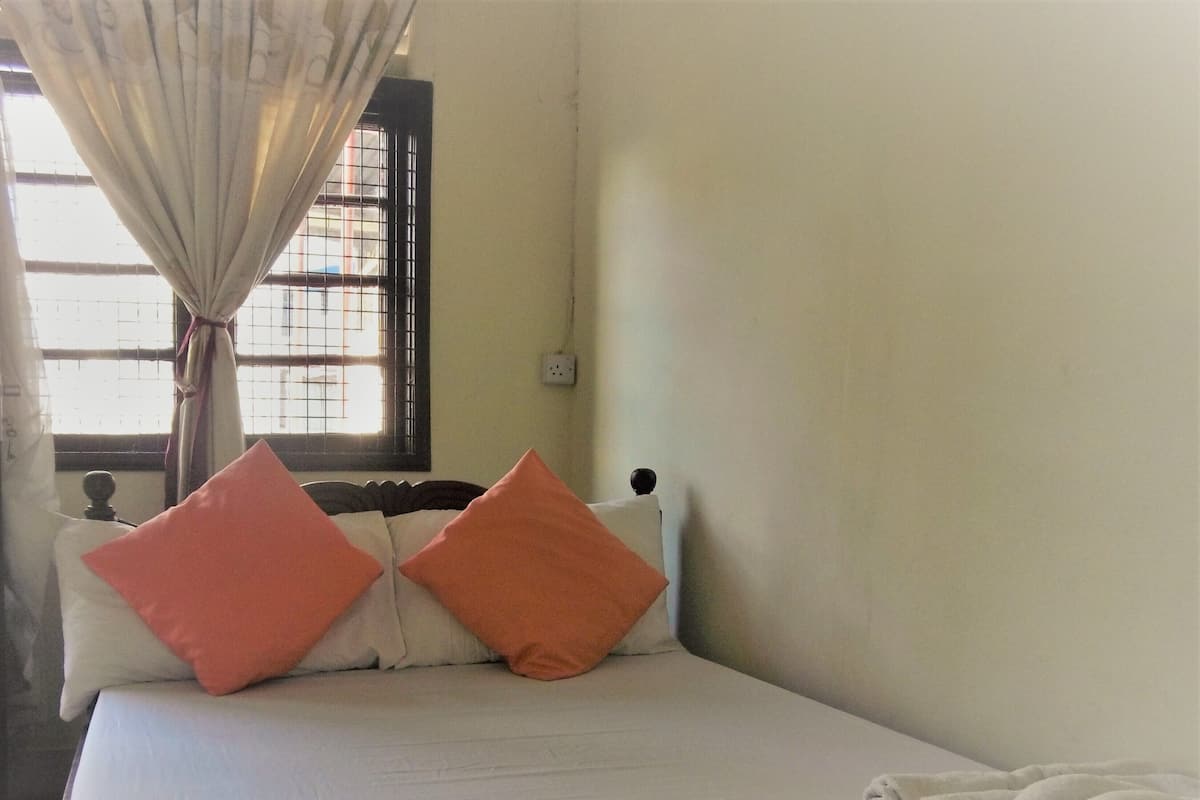 A single bed with two pillows, a window with a curtain, and a wall socket.
