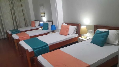 A hotel room with three single beds, each with a teal and orange bedspread, white pillows, and bedside lamps.