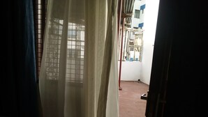 A room with a window covered by a curtain, a red brick floor, and a metal gate outside.