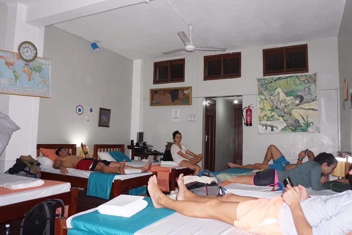 A dormitory room with multiple beds, a ceiling fan, a world map on the wall, and a fire extinguisher.