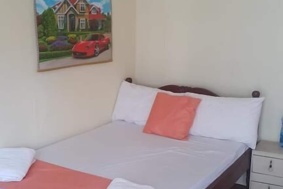 A bedroom with a bed, pillows, a nightstand, a painting, and a rug.