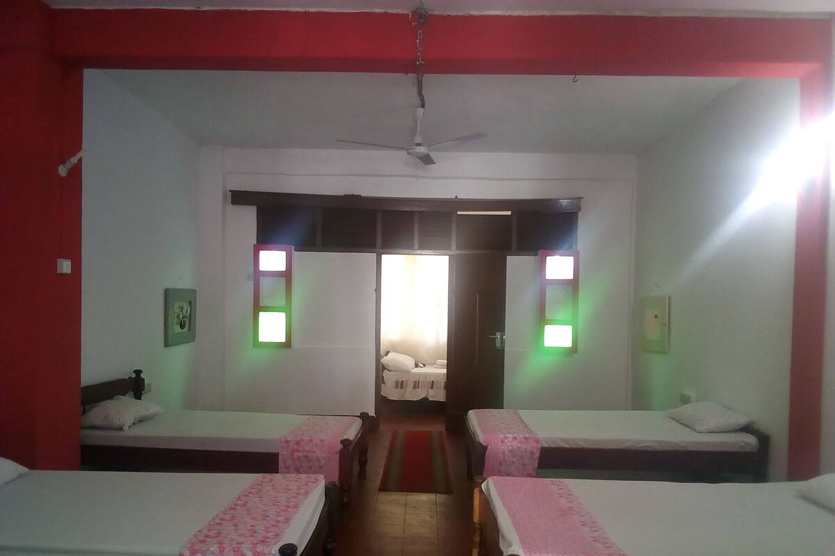 A hotel room with two single beds, a red accent wall, a ceiling fan, and a view through a doorway.