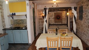 A dining area with a table set for two, a kitchen with blue cabinets, and a stone wall with a decorative plate. -  Good heavens 1, bed & bike, (Betina,Murter)