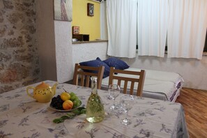 Uma mesa de jantar com toalha de mesa florida, um bule amarelo, uma garrafa de azeite, um prato de frutas e duas taças de vinho.