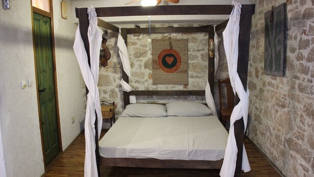 A room with a bed, wooden floor, stone wall, and a green door. -  Good heavens 1, bed & bike, (Betina,Murter)