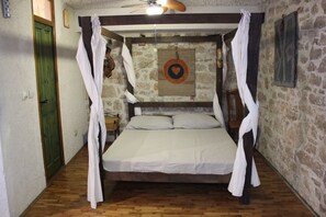 A room with a bed, wooden floor, stone wall, and a green door.
