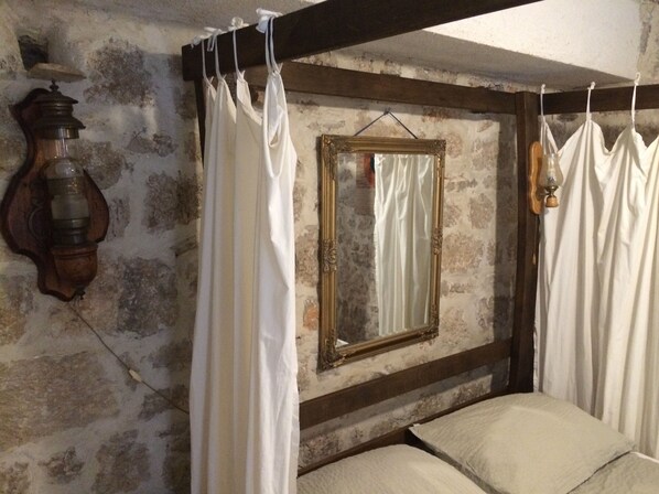 A room with a bed, a wooden headboard, a mirror, and a wall-mounted lamp.