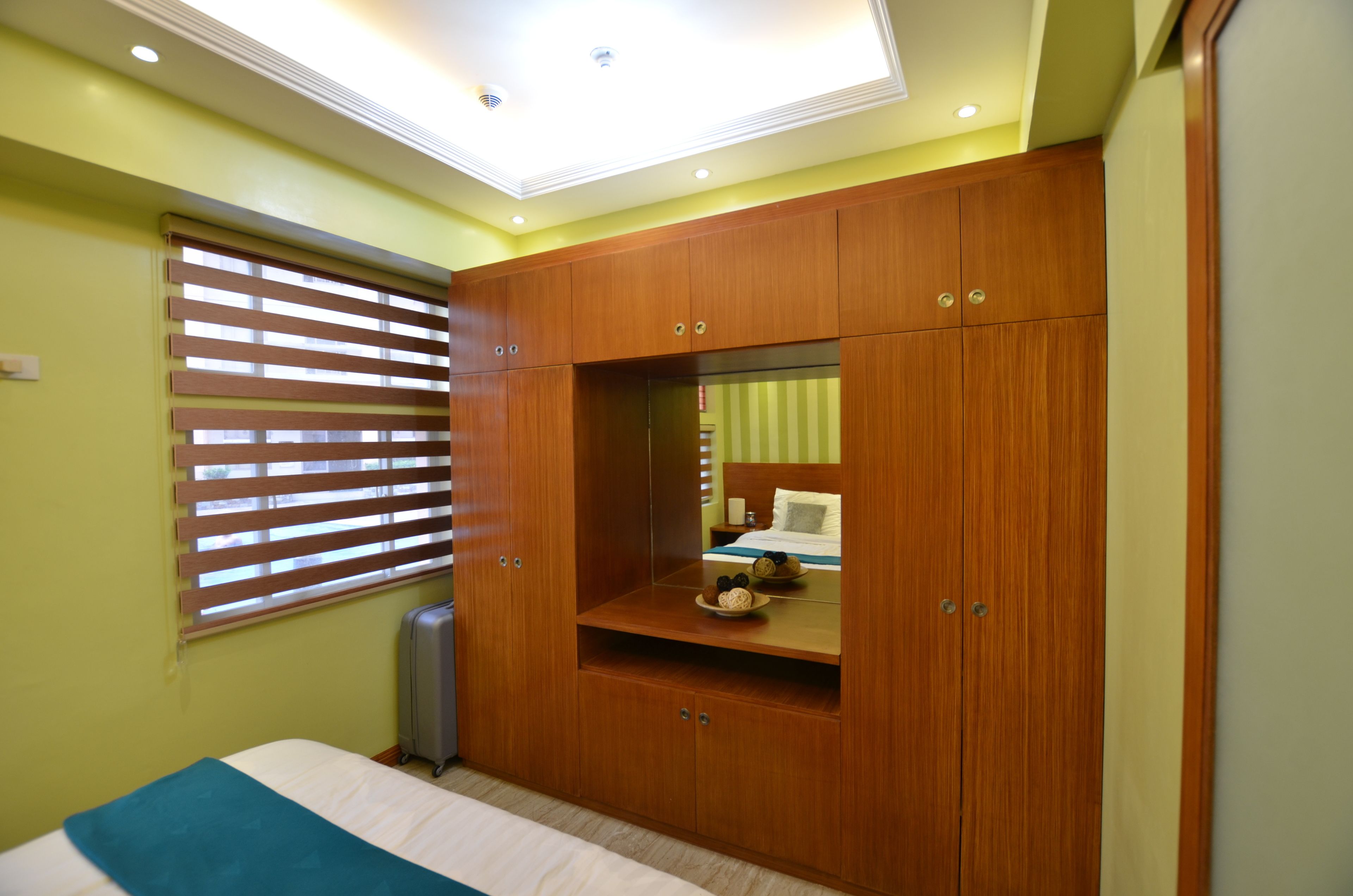 A bedroom with a bed, a wardrobe, a window with blinds, and a ceiling light.