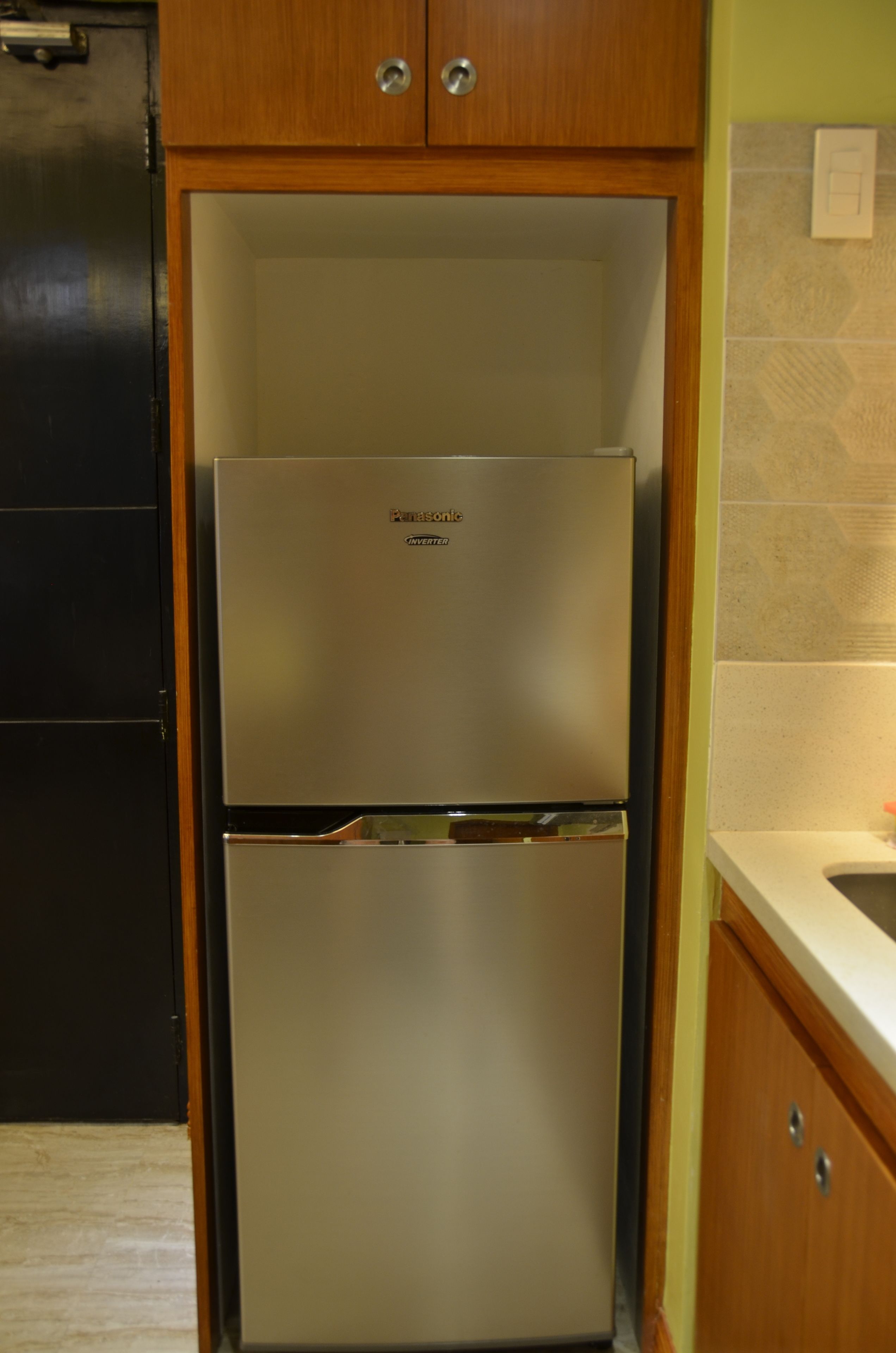 Un frigorífic d'acer inoxidable en una cuina amb armaris de fusta i una barra de resguard rebedor de rajoles.
