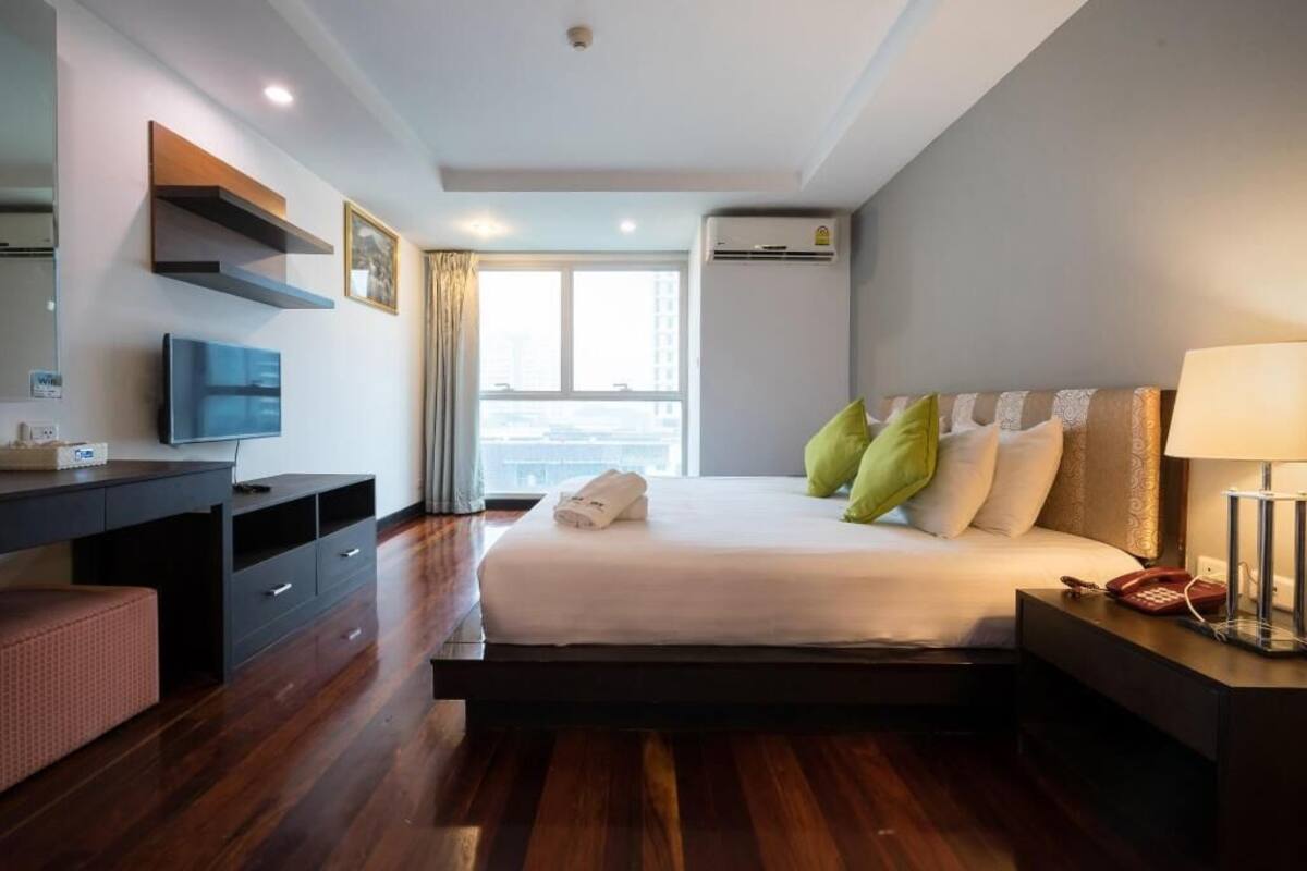 Une chambre d’hôtel comprenant un lit, une table de chevet, une lampe, une télévision et un bureau avec des tiroirs.
