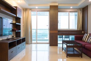 Een moderne woonkamer met een flatscreen televisie, een houten entertainmentkast, een rode bank en een glazen salontafel.