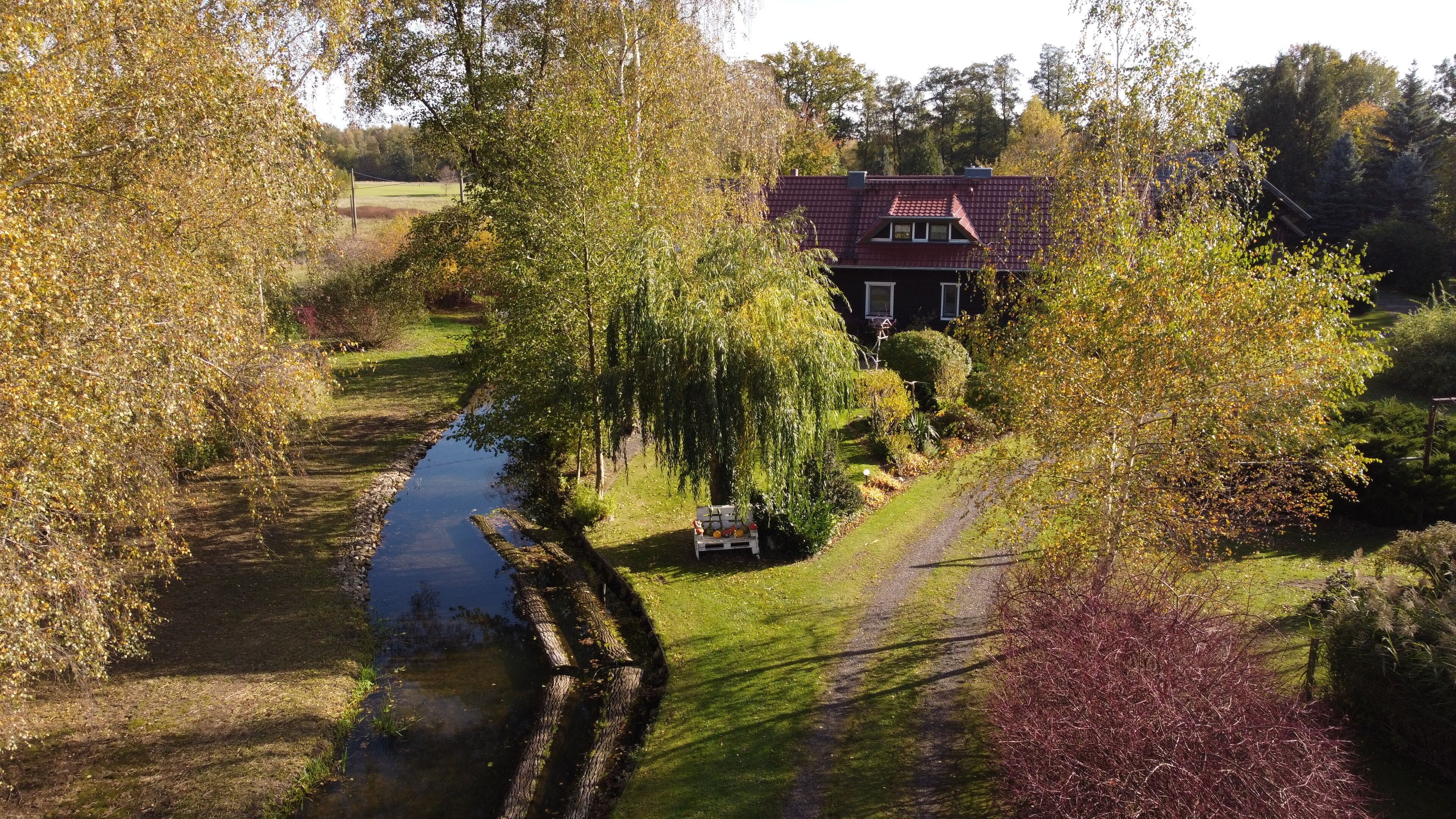A house with a red roof, surrounded by trees and a small stream.