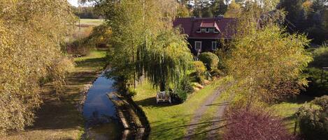A house with a red roof, surrounded by trees and a small stream.