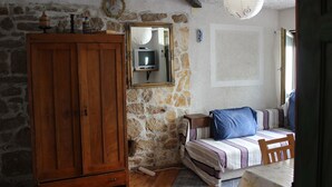 A bedroom with a stone wall, wooden wardrobe, a bed with striped bedding, and a television on a shelf.