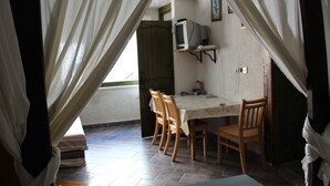 A room with a dining table, chairs, a television on a shelf, and a window with curtains.