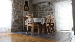 A dining area with a stone wall, wooden chairs, a table with a white tablecloth, and an air conditioning unit.
