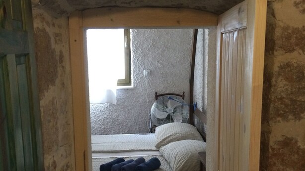 A narrow doorway leading to a small bedroom with a single bed, a wall-mounted fan, and a window.