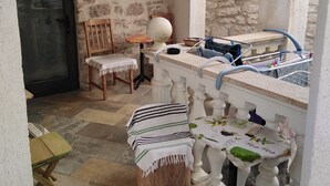 A rustic kitchen with a stone wall, a wooden chair, a small round table, and a bar area with a sink and drying rack.