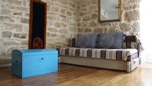 A room with a stone wall, a sofa with striped cushions, a blue chest of drawers, and a mirror on the wall.