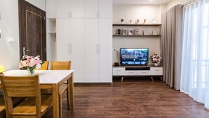 Un salon moderne comprenant un coin repas, un plancher en bois, un téléviseur posé sur un meuble et une grande armoire.