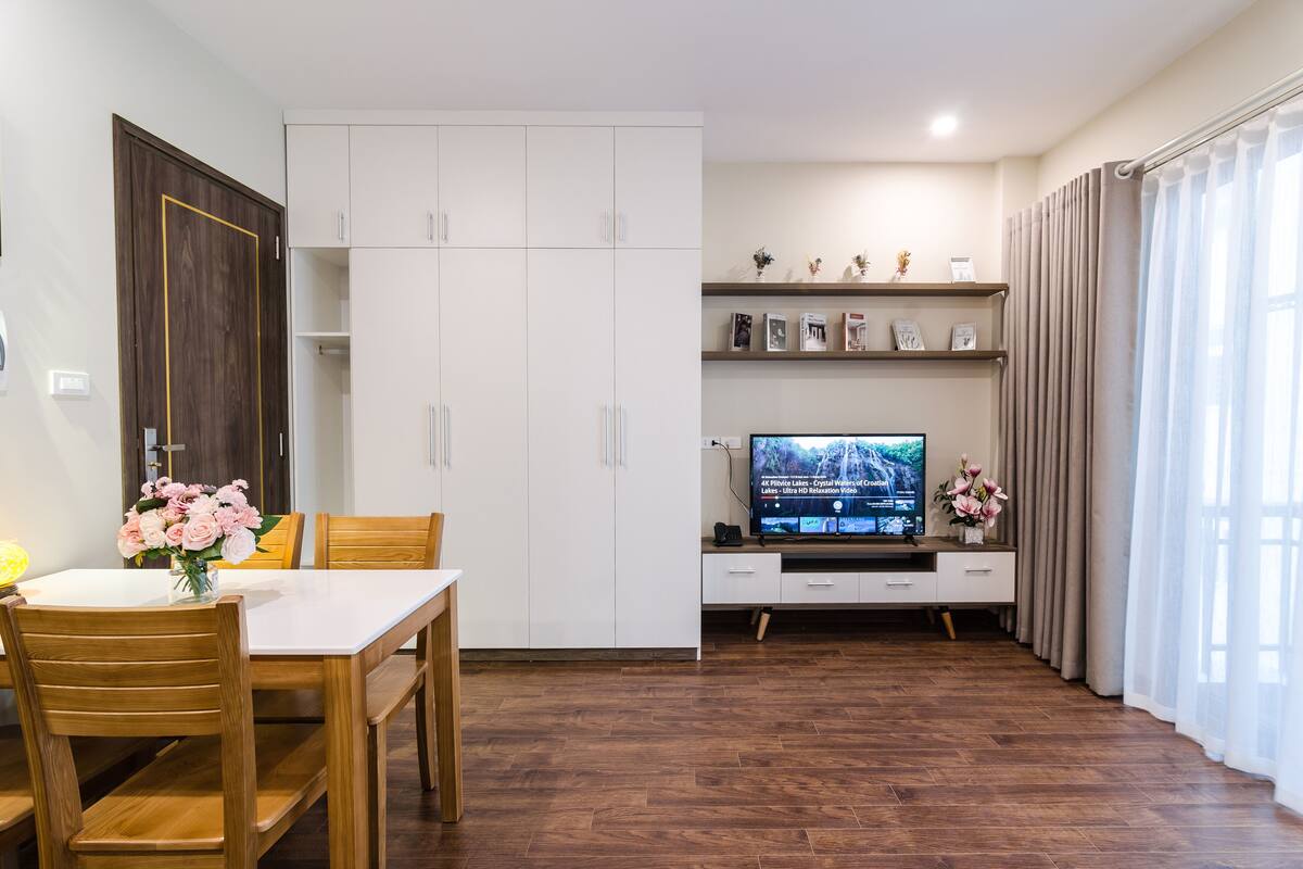 Un salon moderne comprenant un coin repas, un plancher en bois, un téléviseur posé sur un meuble et une grande armoire.