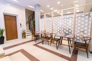 A modern dining area with wooden tables and chairs, a decorative white partition, and a staircase in the background. - Fukurai Boutique Apartments Ha Noi (Hanoi)
