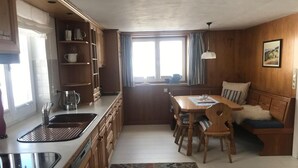 A compact kitchen with a dining area, wooden cabinets, a sink, and a window with curtains.
