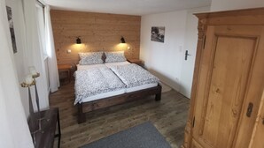 A bedroom with a wooden headboard, two bedside tables, a bed with patterned bedding, a wooden wardrobe, and a door with a handle.