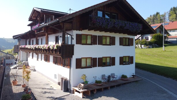A traditional chalet with a balcony, multiple windows, and a gravel driveway.