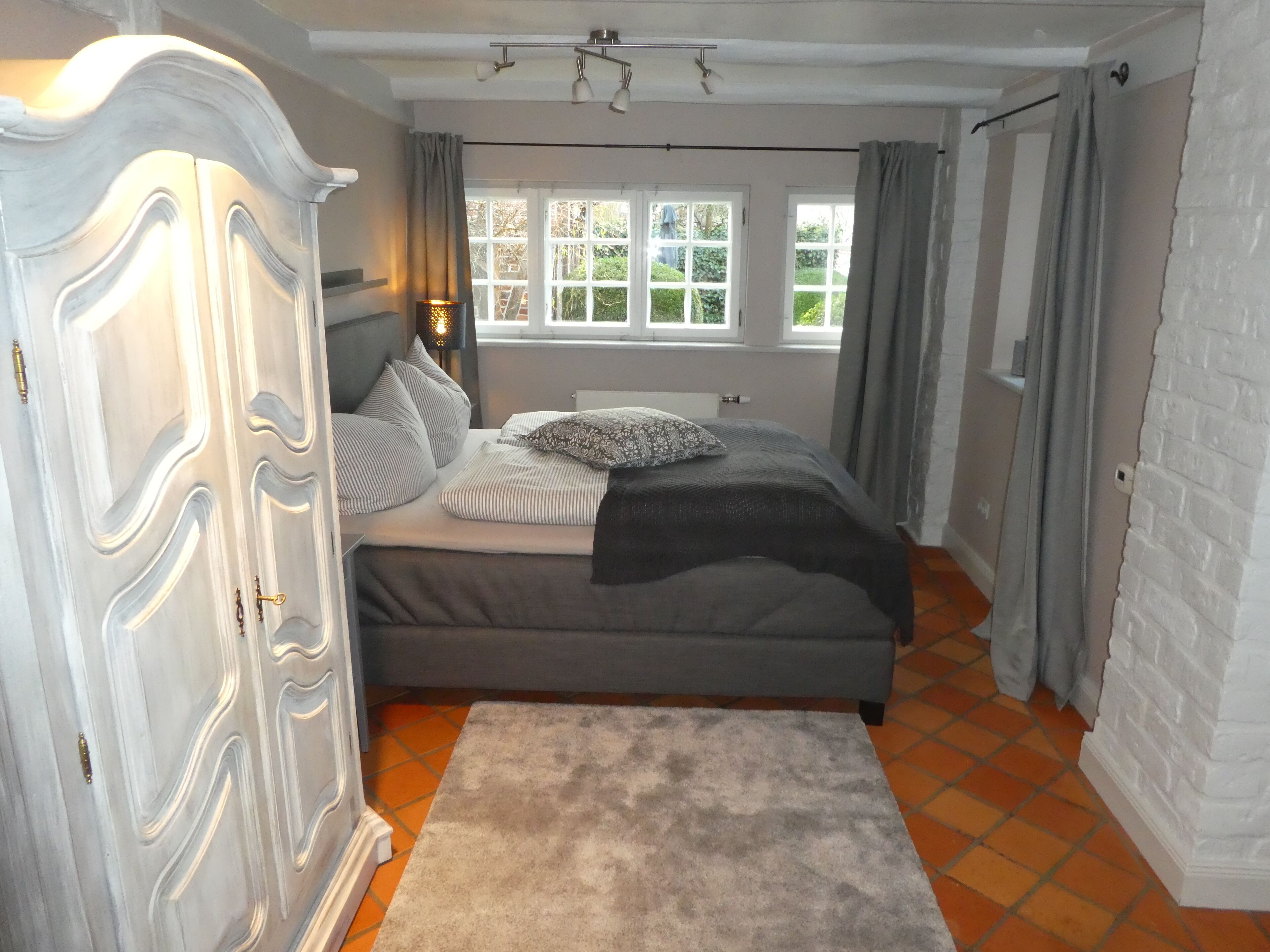 A bedroom with a bed, a wardrobe, a window, and a view of greenery outside.