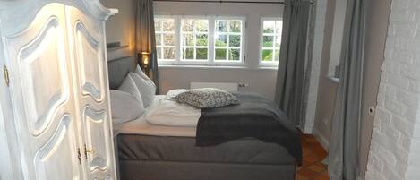 A bedroom with a bed, a wardrobe, a window, and a view of greenery outside.