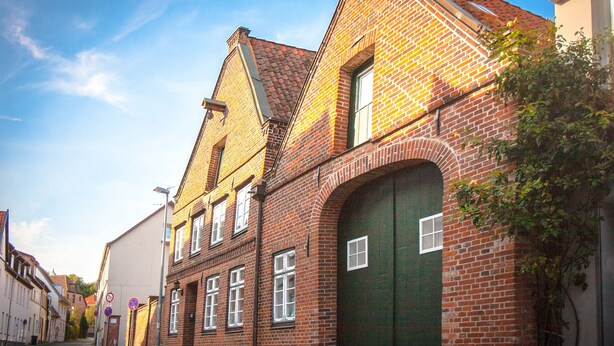 Ein historisches Backsteingebäude mit einer grünen Tür und zahlreichen Fenstern.