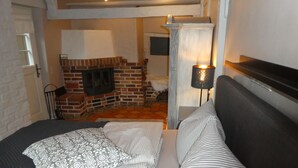 Ein Schlafzimmer mit Kamin aus Backsteinen, einem Bett mit gestreifter Bettwäsche und einem Nachttisch mit Lampe.