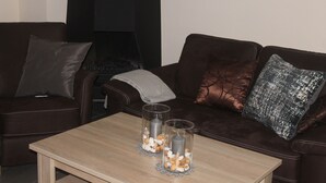A living room with a brown leather sofa, two glass candle holders with candles, and a wooden coffee table. - Modern semi-detached house on the North Sea for up to 4 people (Butjadingen)