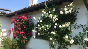 Un edificio blanco con tejado de tejas y un jardín con rosas rosadas y blancas.