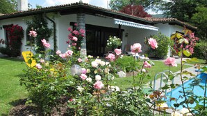 Una casa con jardín lleno de rosas rosadas, piscina y un camino de piedra.