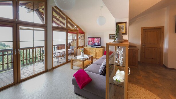 Un espacio habitable amplio con balcón, un sofá, un televisor y un aparador de vidrio con objetos decorativos.