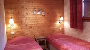 A wooden cabin room with two beds, each with pink bedding. There are wall-mounted lights and a small shelf with framed photos. - Magnificent spacious apartment with WIFI, ideal for PMR. 3-star rating. (Xonrupt-Longemer)