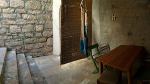A stone-walled room with a wooden table and chairs, a woven mat hanging on the wall, and a small shelf with a decorative item. - Fischer Fritz, bed & bike (Betina;Murter)