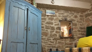 A room with a stone wall, a blue wardrobe, a bed with a yellow cover, and a mirror reflecting a colorful curtain. - Fischer Fritz, bed & bike (Betina;Murter)