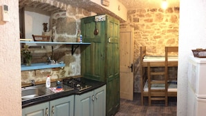 A rustic kitchen with stone walls, wooden cabinets, and a wooden dining table. - Fischer Fritz, bed & bike (Betina;Murter)