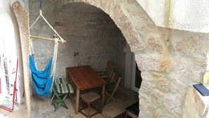 A stone-walled room with a wooden table and chairs, a hammock, and a small wooden chest. - Fischer Fritz, bed & bike (Betina;Murter)