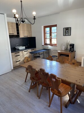 A modern kitchen with wooden cabinets, a dining table with chairs, a built-in oven, and a window with a view.
