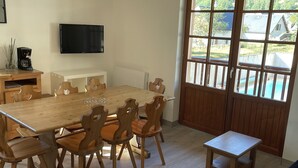 A dining area with a wooden table and chairs, a television mounted on the wall, and a window with a view of the outdoors. - Rental three-room apartment in Saint Lary (Vignec)