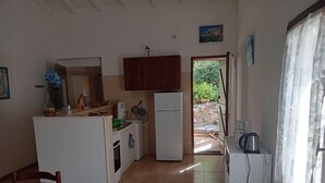 Eine kleine Küche mit Kühlschrank, Herd und Spüle. Ein Esstisch mit Stühlen und ein Fenster mit Vorhängen sind ebenfalls vorhanden.