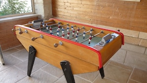 A wooden foosball table with metal rods and figures, set on a tiled floor in a room with wooden walls and a window.