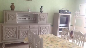 A dining area with a table and chairs, a cabinet with decorative carvings, a television, and a vase on the cabinet.