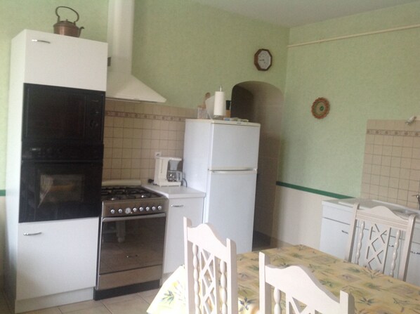 Cocina compacta con estufa, horno y refrigerador blanco. Hay una mesa de comedor con sillas y una cafetera pequeña.
