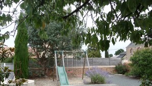 A playground with a slide and swings, surrounded by trees and a gravel area.